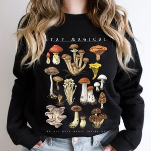 Op de afbeelding: Zwart sweatshirt met een paddenstoelprint en de tekst "Stay Magical" en "We all have magic inside us".
