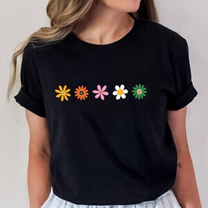 May include: A black t-shirt with a row of five colorful flowers printed on the front. The flowers are in shades of orange, yellow, pink, white, and green.