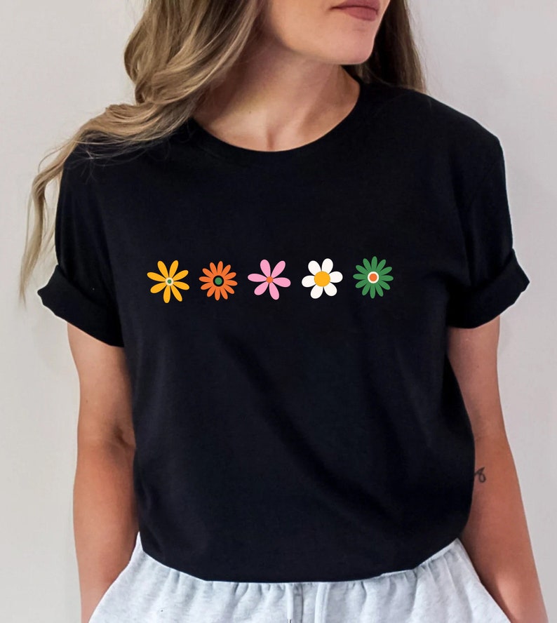 May include: A black t-shirt with a row of five colorful flowers printed on the front. The flowers are in shades of orange, yellow, pink, white, and green.