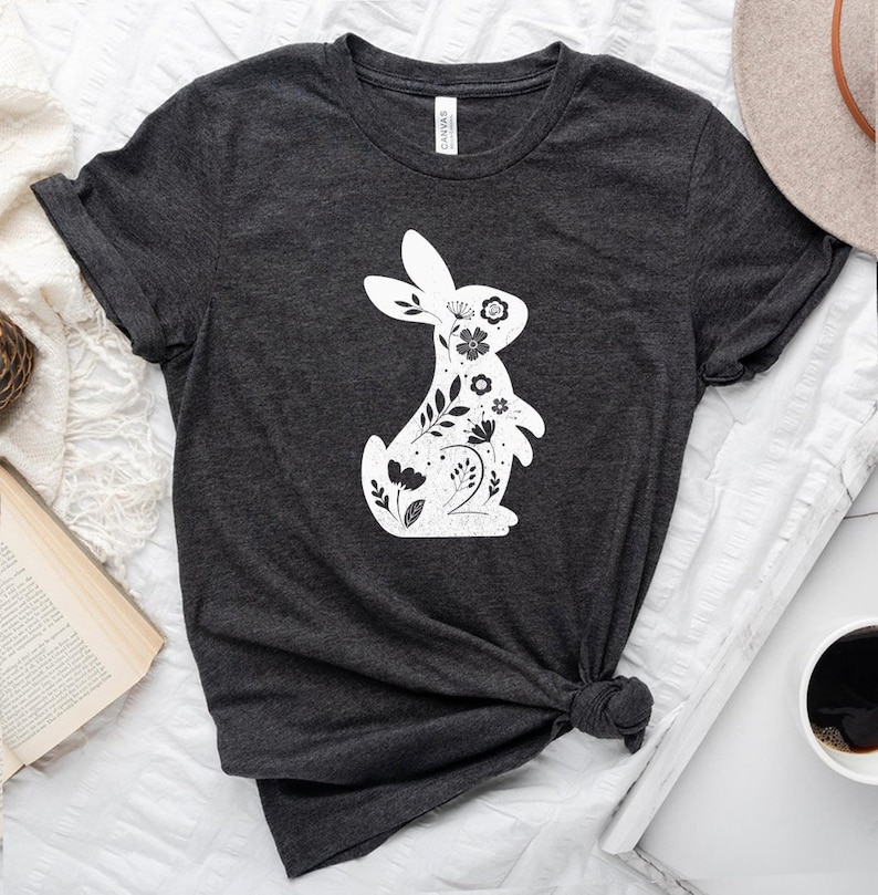 K&ouml;nnte beinhalten: Ein dunkelgraues T-Shirt mit einer wei&szlig;en Silhouette eines Kaninchens mit floralen Designs innerhalb der Silhouette.
