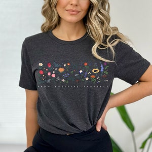 May include: A dark grey t-shirt with a floral design and the text "Grow Positive Thoughts".