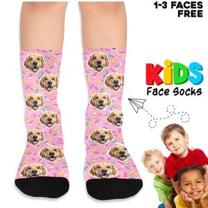 May include: Pink socks with a repeating pattern of golden retriever faces and colorful sprinkles. The socks have black toes and the text "KIDS Face Socks" is displayed in colorful letters. The image also includes the text "1-3 FACES FREE".