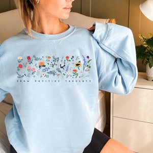 May include: A light blue sweatshirt with a floral design and the text "Grow Positive Thoughts".