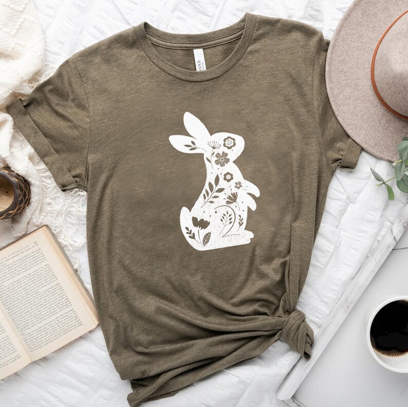 K&ouml;nnte beinhalten: Ein gr&uuml;nes T-Shirt mit einem wei&szlig;en floralen Hasendesign. Der Hase besteht aus Blumen und Bl&auml;ttern.