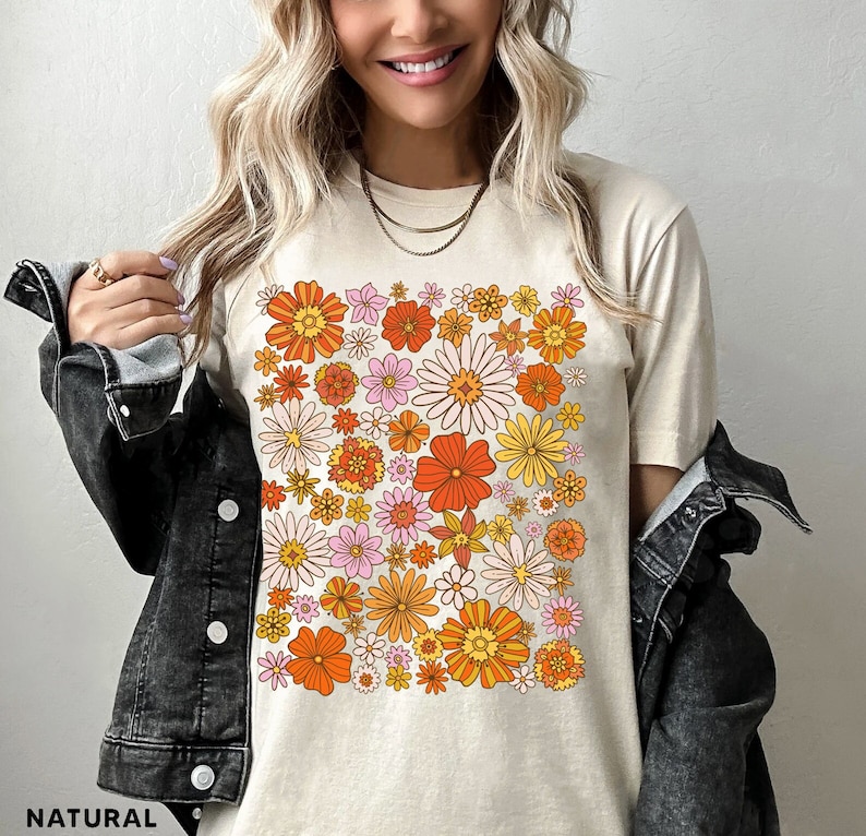 May include: A beige t-shirt with a retro floral print featuring orange, yellow, pink, and white flowers. The shirt has a crew neck and short sleeves.