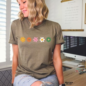 May include: A green t-shirt with a row of five colorful flowers printed on the front. The flowers are orange, orange, pink, white, and green.