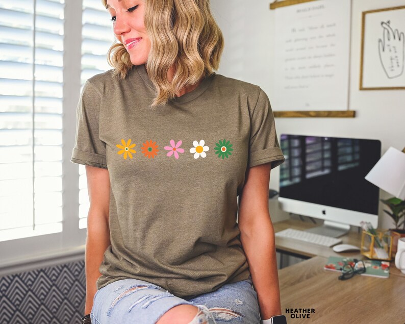 May include: A green t-shirt with a row of five colorful flowers printed on the front. The flowers are orange, orange, pink, white, and green.