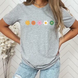 May include: A gray t-shirt with a row of five colorful flowers printed on the front. The flowers are orange, orange, pink, white, and green.