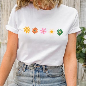 May include: White t-shirt with a row of five colorful flowers printed on the front. The flowers are yellow, orange, pink, white, and green.
