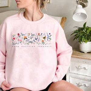 May include: Pink sweatshirt with a floral design and the text "Grow Positive Thoughts" printed on the front.
