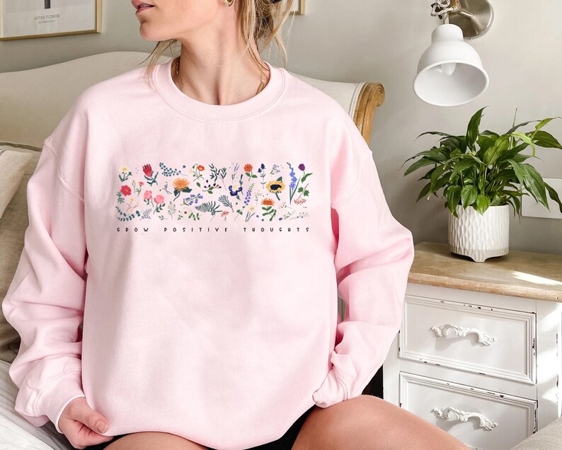 May include: Pink sweatshirt with a floral design and the text "Grow Positive Thoughts" printed on the front.