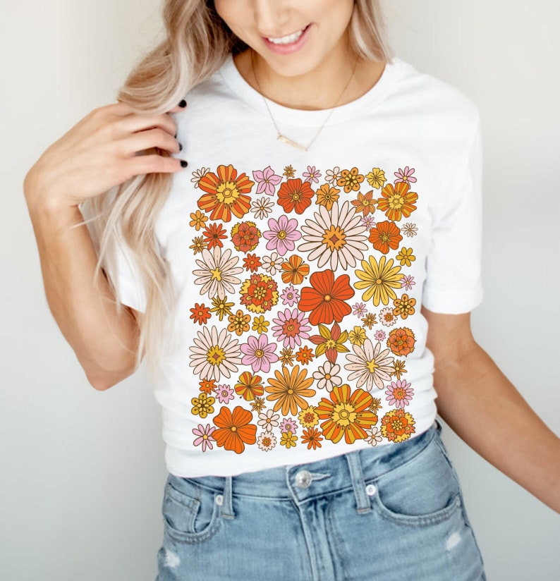 May include: White t-shirt with a colorful floral pattern in shades of orange, yellow, pink, and white. The flowers are arranged in a dense, repeating pattern.