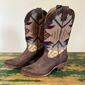 May include: A pair of brown leather cowboy boots with a geometric patterned fabric shaft. The boots have a pointed toe and a low heel.