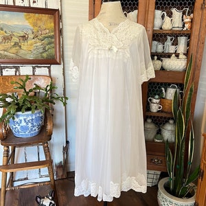 May include: A white sheer nightgown with lace trim and a bow at the neckline. The nightgown is on a mannequin and is displayed against a wooden background.
