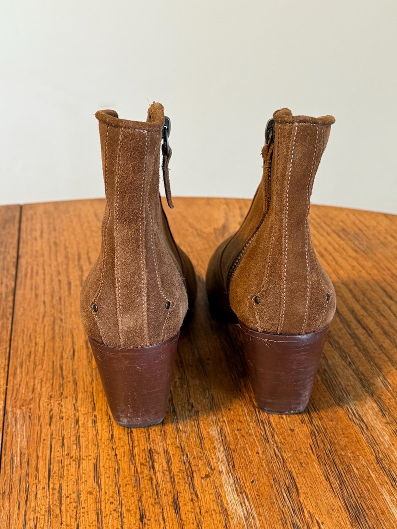 May include: A pair of brown suede ankle boots with a stacked heel. The boots have a zipper on the side and decorative stitching. The heels are approximately 3 inches tall.