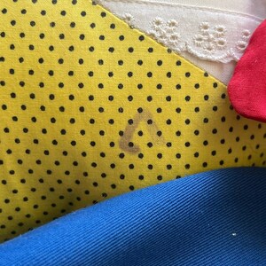 K&ouml;nnte beinhalten: Nahaufnahme eines gelben Stoffes mit schwarzen Punkten. Der Stoff ist &uuml;ber einen blauen Stoff und einen wei&szlig;en Stoff mit Spitzenbesatz gefaltet. Auf dem gelben Stoff befindet sich ein brauner Fleck.