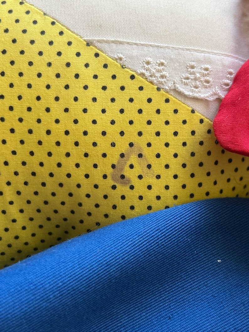 K&ouml;nnte beinhalten: Nahaufnahme eines gelben Stoffes mit schwarzen Punkten. Der Stoff ist &uuml;ber einen blauen Stoff und einen wei&szlig;en Stoff mit Spitzenbesatz gefaltet. Auf dem gelben Stoff befindet sich ein brauner Fleck.