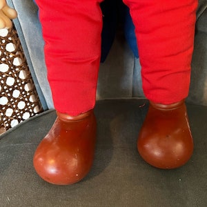 K&ouml;nnte beinhalten: Eine rote Hose mit blauen Bes&auml;tzen und braunen Schuhen. Die Hose ist aus weichem, pl&uuml;schigem Stoff und die Schuhe aus hartem, plastischem Material.