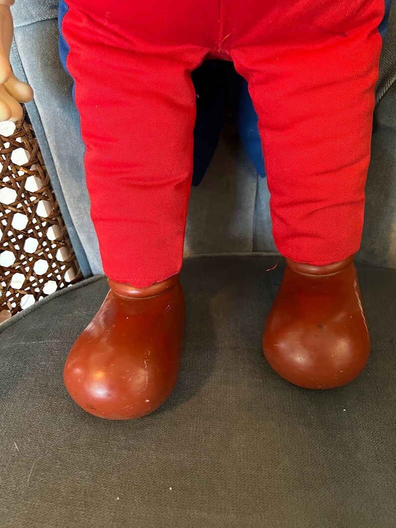 K&ouml;nnte beinhalten: Eine rote Hose mit blauen Bes&auml;tzen und braunen Schuhen. Die Hose ist aus weichem, pl&uuml;schigem Stoff und die Schuhe aus hartem, plastischem Material.