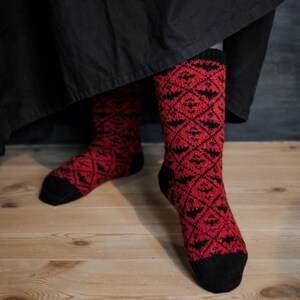 Könnte beinhalten: Ein Paar rot-schwarze gemusterte Socken mit geometrischem Design. Die Socken sind aus einem weichen, warmen Material gefertigt und perfekt für kaltes Wetter.