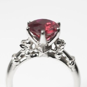 May include: A silver ring with a red gemstone and intricate details. The ring has a star-shaped design with small accents on the band.