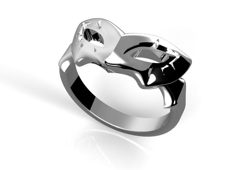 May include: A silver ring featuring a mask design. The mask is stylised and has a geometric pattern.