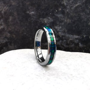 May include: A silver tungsten carbide ring with a thin band of green and blue opal inlay. The ring is engraved with "Tungsten Carbide" on the inside of the band.