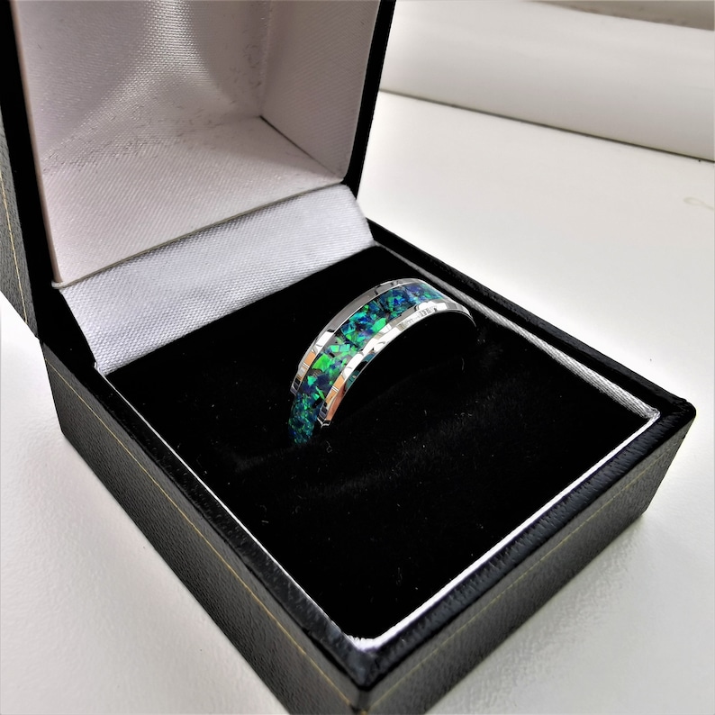 May include: A silver ring with a green and blue opal inlay. The ring is in a black ring box.