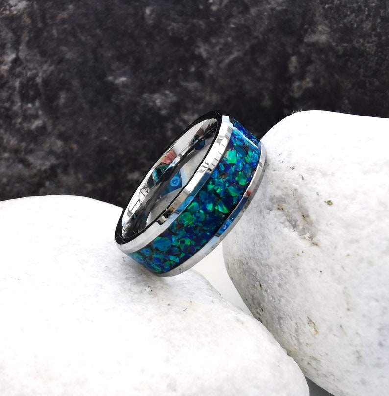 May include: A silver ring with a blue and green inlay. The ring is made of tungsten carbide and has a polished finish.