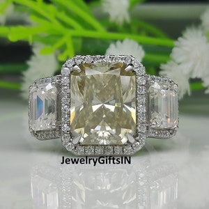 May include: A silver ring with a large, rectangular, light yellow gemstone surrounded by smaller diamonds. The ring has two smaller, rectangular, clear gemstones on either side of the center stone.