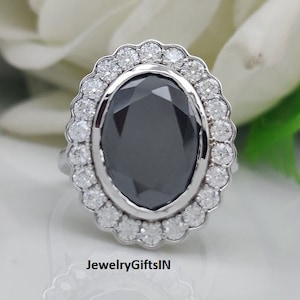 Puede incluir: Un anillo de plata con una gran piedra negra ovalada rodeada por un halo de piedras blancas más pequeñas.