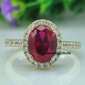 Può includere: Un anello d'oro con un grande rubino ovale circondato da un'aureola di diamanti più piccoli. La fascia è anche incastonata con diamanti più piccoli.