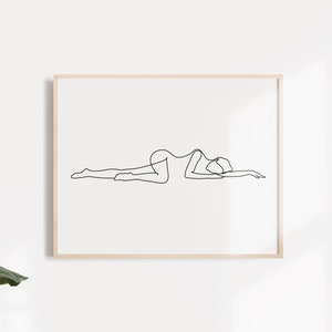 May include: A black and white line drawing of a person lying on their stomach with their head turned to the side. The drawing is framed in a light wood frame.