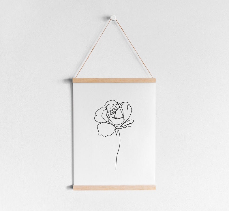 May include: A black and white line drawing of a single rose on a white background. The drawing is framed with a natural wood frame and hanging on a white wall.