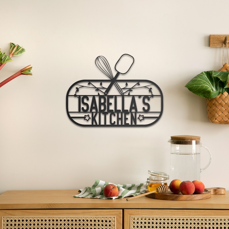 May include: Black metal kitchen sign with the text "Isabella's Kitchen" and a crossed whisk and spatula.