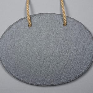 May include: Oval-shaped gray slate sign with a textured surface, suspended by two natural-colored rope loops. The sign is blank, offering space for custom text or designs. The background is a solid light gray.