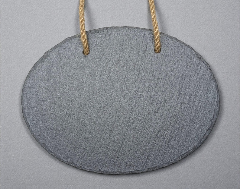 May include: Oval-shaped gray slate sign with a textured surface, suspended by two natural-colored rope loops. The sign is blank, offering space for custom text or designs. The background is a solid light gray.