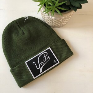 May include: A green beanie with a black patch that says "Unity" in white cursive lettering.