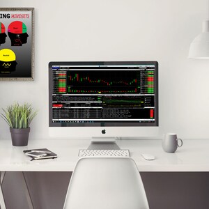 以下が含まれることがあります： コンピュータ、キーボード、マウス、マグカップ、植物、そして「Trading Mindsets」と書かれた額縁に入ったポスターが置かれた白い机。