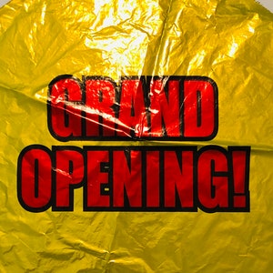 May include: A gold foil balloon with the text "GRAND OPENING!" in red letters.