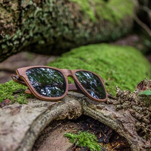 Peut inclure: Lunettes de soleil en bois avec des verres fonc&eacute;s reposant sur une b&ucirc;che recouverte de mousse dans un environnement forestier.