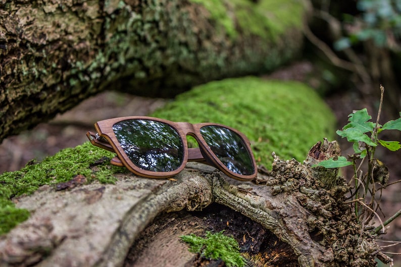 Peut inclure: Lunettes de soleil en bois avec des verres fonc&eacute;s reposant sur une b&ucirc;che recouverte de mousse dans un environnement forestier.