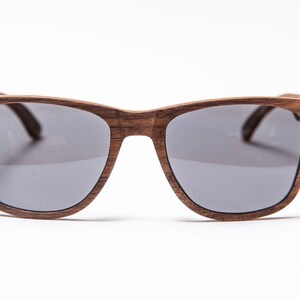 Peut inclure: Une paire de lunettes de soleil en bois brun avec des verres gris. Les lunettes ont une forme rectangulaire simple.