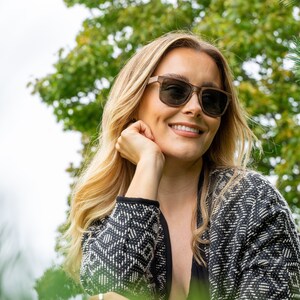 Peut inclure: Une femme aux cheveux blonds portant des lunettes de soleil brunes et un cardigan &agrave; motifs noir et blanc.