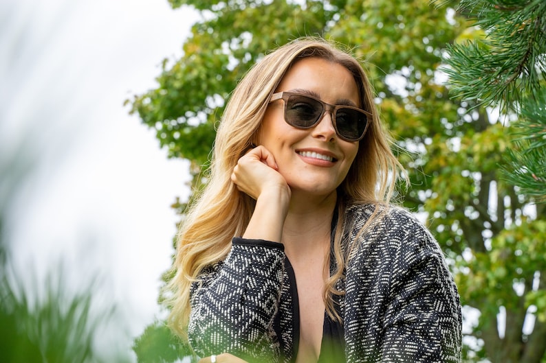 Peut inclure: Une femme aux cheveux blonds portant des lunettes de soleil brunes et un cardigan &agrave; motifs noir et blanc.