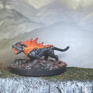 May include: A miniature figurine of a black feline creature with a fiery orange mane and accents. The figurine is posed on a circular base with a rocky texture, set against a backdrop of a mountain landscape.