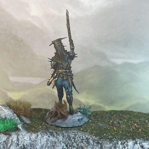 May include: Miniature figure of a warrior in dark armor, holding a wooden staff aloft. The figure stands on a small rock with a miniature landscape background. The armor is detailed with spikes and a chain around the waist.