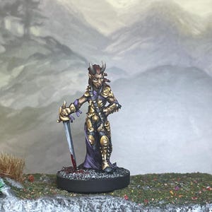 Puede incluir: Figura de fantasía en miniatura de un guerrero humanoide con cuernos, con armadura dorada y túnicas moradas, sosteniendo una espada con una hoja ensangrentada. La figura se alza sobre una base circular, sobre un fondo de paisaje montañoso brumoso.