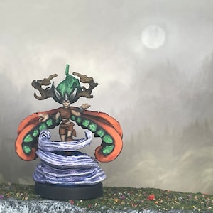 May include: A miniature fantasy figure of a female character with green hair and a brown outfit, standing on a purple and white swirling base. The figure has orange and green wings and is set against a misty, mountainous backdrop.