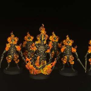 May include: Miniature figurines of fiery figures, painted in orange, yellow, and black. Flames are depicted around their heads and bodies. Each figure is holding a weapon, and they are set on black bases.